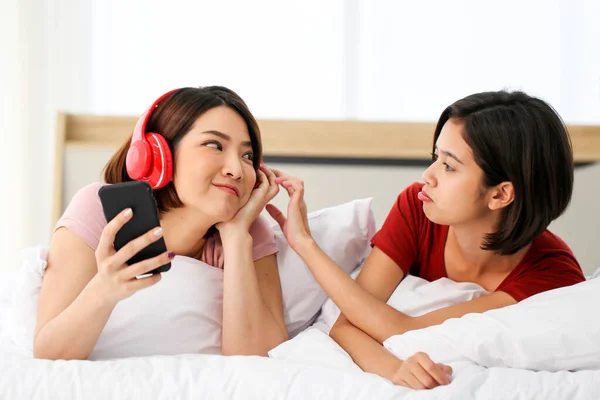 快乐的亚洲女人戴着耳机 喜欢在卧室里玩手机和平板电脑的音乐 — 图库照片
