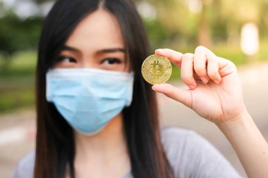 Yüz koruması takan Asyalı kadın, Virüs maskeli bitcoin madeni para sorunu, Coronavirus sırasında ekonomik kriz, Covid-19 salgını, odak seçici.