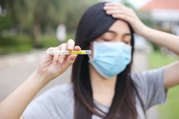 Asian woman  wearing face protection Holding a thermometer Temperature measurement,Virus mask,Healthcare and sickness prevention from coronavirus, Covid19,Selective of focus.