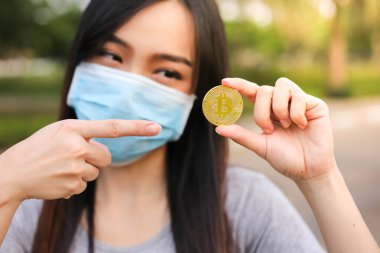 Yüz koruması takan Asyalı kadın, Virüs maskeli bitcoin madeni para sorunu, Coronavirus sırasında ekonomik kriz, Covid-19 salgını, odak seçici.