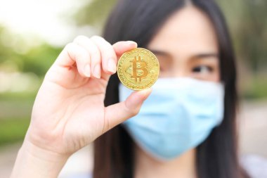 Yüz koruması takan Asyalı kadın, Virüs maskeli bitcoin madeni para sorunu, Coronavirus sırasında ekonomik kriz, Covid-19 salgını, odak seçici.