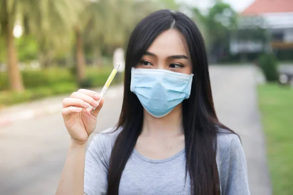 Asian woman  wearing face protection Holding a thermometer Temperature measurement,Virus mask,Healthcare and sickness prevention from coronavirus, Covid19,Selective of focus.