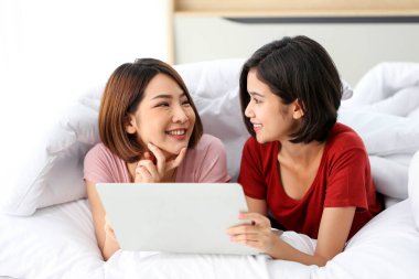 Mutlu çift Asyalı kadın kulaklık takıyor ve yatak odasında cep telefonu ve tablet çalan müziklerden hoşlanıyor..