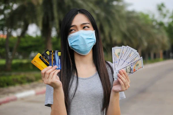 Yüz koruması takan Asyalı kadın, Virüs maskesi para ve kredi kartı problemi, Coronavirus sırasında ekonomik kriz, Covid-19 pandemisi