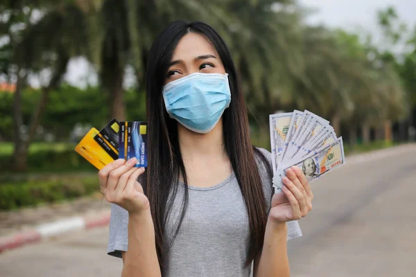 Asian woman  wearing face protection ,Virus mask  Holding money and credit card financial problem,economic depression during the Coronavirus,Covid-19 pandemic