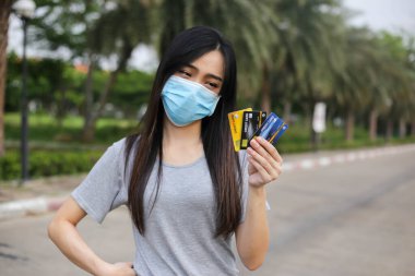Yüz koruması takan Asyalı kadın, Virüs maskesi para ve kredi kartı problemi, Coronavirus sırasında ekonomik kriz, Covid-19 pandemisi