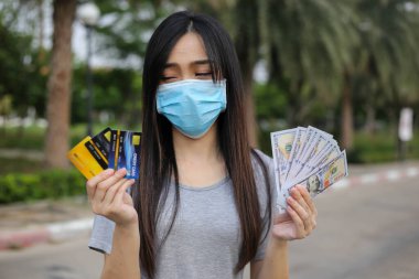 Yüz koruması takan Asyalı kadın, Virüs maskesi para ve kredi kartı problemi, Coronavirus sırasında ekonomik kriz, Covid-19 pandemisi