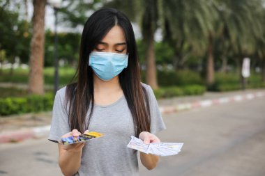 Yüz koruması takan Asyalı kadın, Virüs maskesi para ve kredi kartı problemi, Coronavirus sırasında ekonomik kriz, Covid-19 pandemisi