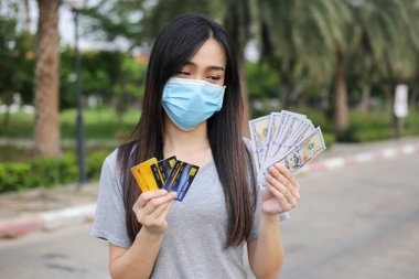 Yüz koruması takan Asyalı kadın, Virüs maskesi para ve kredi kartı problemi, Coronavirus sırasında ekonomik kriz, Covid-19 pandemisi