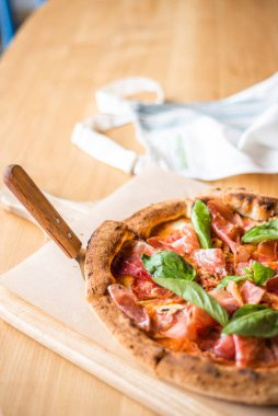 Delicious pizza stands on the table, pizza with red sauce, pancetta and basil, Italian cuisine, pizzeria