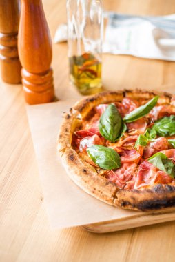 Delicious pizza stands on the table, pizza with red sauce, pancetta and basil, Italian cuisine, pizzeria