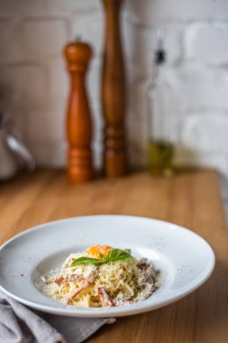 Pancetta 'lı spagetti carbonara, ahşap masada beyaz kasede yumurta ve peynir.