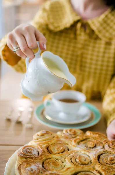 Woman pouring milk into cup with aromatic tea on table. Synabons are on the table. Tea time — Stock Photo, Image