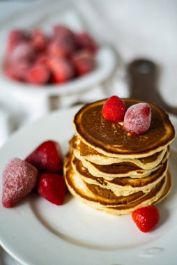 Yakın plan leziz krepler, arka planda çilek ve şurup var. Tatlı şurup bir krep yığınından akar.