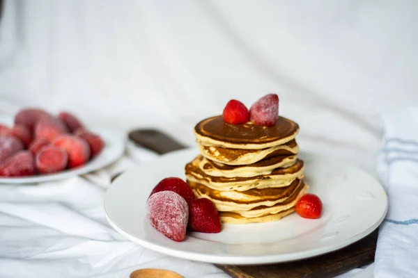Close-up heerlijke pannenkoeken, met aardbeien en siroop op een lichte achtergrond. Zoete siroop stroomt uit een stapel pannenkoeken — Stockfoto