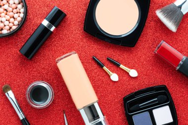 Cosmetics on a red background: lipstick, eyeshadow, powder, blush, eyeliner, makeup brushes, foundation, lip gloss