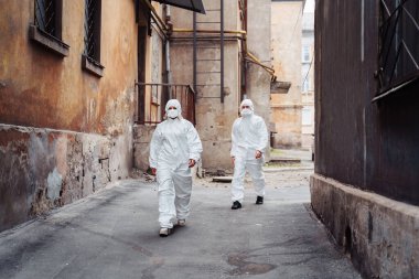 Koruyucu giysileri ve solunum cihazları olan insanlar savaş sırasında terk edilmiş, terk edilmiş ve harap olmuş caddelerde yürüyorlar. Coronavirus konsepti.