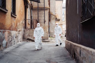 Koruyucu giysileri ve solunum cihazları olan insanlar savaş sırasında terk edilmiş, terk edilmiş ve harap olmuş caddelerde yürüyorlar. Coronavirus konsepti.