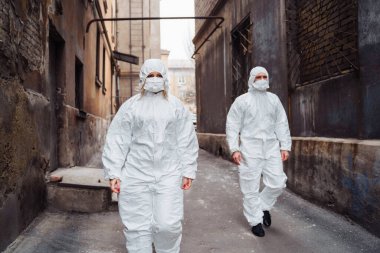 Koruyucu giysileri ve solunum cihazları olan insanlar savaş sırasında terk edilmiş, terk edilmiş ve harap olmuş caddelerde yürüyorlar. Coronavirus konsepti.