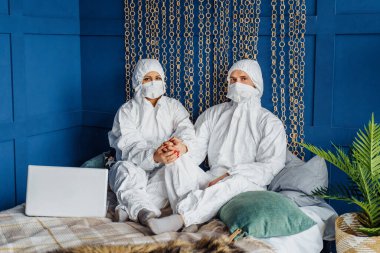 Kendine dikkat et ve evde kal! Doktorlar yatakta oturup kameraya bakıyorlar, koronavirüse karşı maske takıyorlar. Koruyucu giysili insanlar covid-19 salgınından dolayı izole edilmiş.