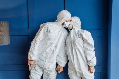Kendine dikkat et! Duvarın yanında dikilen ve Coronavirus 'a karşı maske takan iki genç doktor. Koruyucu giysili insanlar, covid-19 salgını nedeniyle izole bir şekilde evlerinde kalıyorlar.