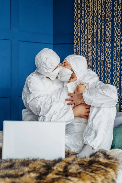 Twee Mensen Beschermende Pakken Gezichtsmaskers Zittend Het Bed Elkaar Kussen — Stockfoto