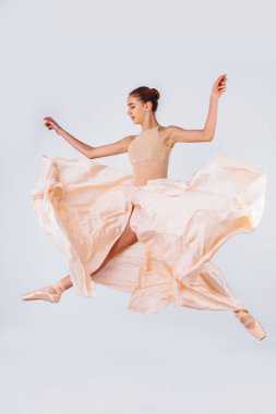 Bedava uçuş. Beyaz stüdyo arka planında dans eden zarif klasik balerin. Pastel bej kumaş. Zarafet, sanatçı, hareket, aksiyon ve hareket konsepti. Ağırlıksız ve esnek görünüyor. Moda.