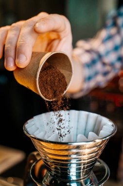 Dikey görüntü. Alternatif Kahve Hazırlama Yöntemi. Barista 'nın ellerine yakın çekim, kahve filtresine küçük bir fincandan kahve dökmek.