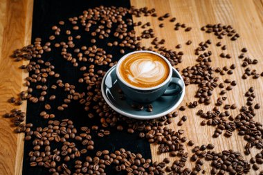 Kahverengi ve siyah masada kahve fincanı dökülmüş kahve çekirdekleri arasında. Kafede kahve sanatıyla kapuçino..