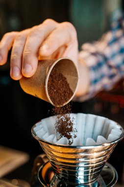 Dikey görüntü. Alternatif Kahve Hazırlama Yöntemi. Barista 'nın ellerine yakın çekim, kahve filtresine küçük bir fincandan kahve dökmek.