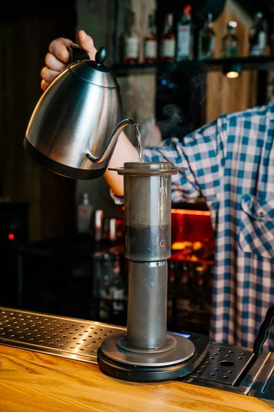 Alternative Coffee Brewing Method. Close-up of barista hand pouring water from the kettle to coffee filter aeropress in the restaurant.