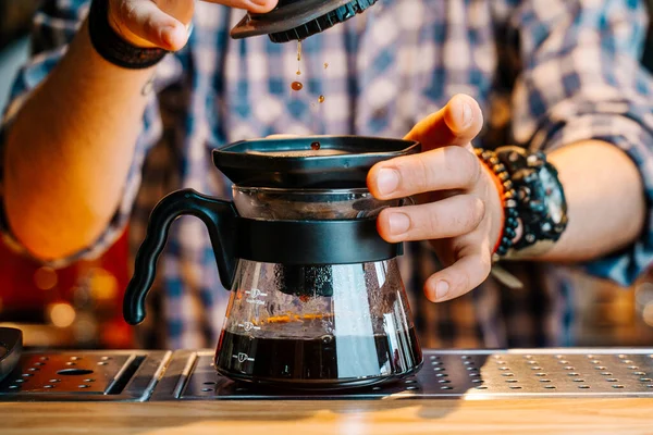 Alternative Coffee Brewing Method. Close-up of the hands of barista who is preparing filter coffee in an aeropress. Barista wears a checkered flannel shirt and works at the bar counter.