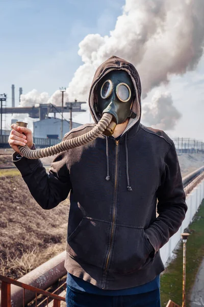 Bad ecology. Man in gas mask on background of a smoking metallurgical plant in industrial zone and and keeps the hose from the gas mask from which the smoke comes. Escape from ecological catastrophy