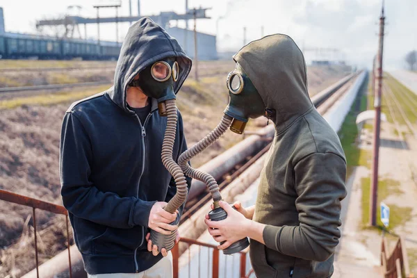 Bad ecology. Two men friends in the old model gas masks stand againts the background of a smoking metallurgical plant and look at each other. People trying to escape from ecological catastrophy