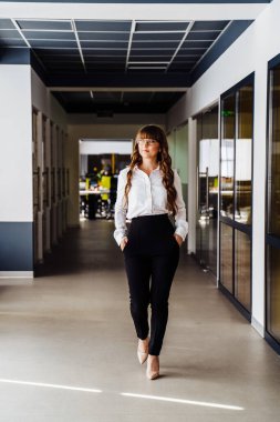Güzel, kendine güveni tam bir iş kadını. Günlük beyaz gömlek ve siyah pantolon giymiş. Ofiste dolanıp etrafa bakıyor. Yeni Çalışma Alanı Keşfediliyor