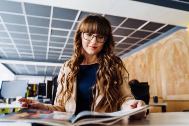 Kendine güvenen, zeki, iş kadını çalışma odasındaki evraklarla çalışıyor. Masada oturuyor, koyu mavi bir elbise ve kahverengi bir ceket giyiyor. Gözlük takıyor ve çok zeki görünüyor.