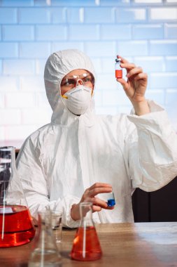Biological hazard. Epidemic of the Chinese coronavirus. An asian woman in a protective suit and mask holds an injection syringe and vaccine. Vaccine from, flu, coronavirus, ebola, TB.