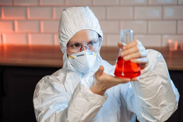 Research and development concept. Close-up of young female laboratory worker holding test tubes with red chemists wearing a protective white suit