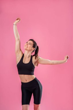 Çekici kaslı kız sabah egzersizleri yapıyor, tatlı tatlı esniyor, hayal kuruyor ve gülümsüyor. Stüdyoda eğitim hareketleri gösteriliyor. Pembe arka planda izole edilmiş, siyah bluz ve tavalar giyiyor..