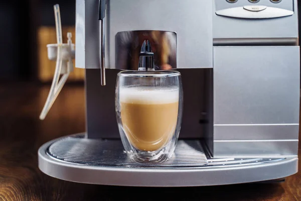 Making fresh coffee going out from a coffee espresso machine. Making capuccino in glass transparent coffee cup. Budget coffee maker