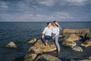 Düşük ihtimal. Mavi bulutlu gökyüzüne karşı denizde taşların üzerinde duran parlak elbiseli çekici bir çift. Yumuşak akşam güneşinin altında. Dört gözle bekliyorum, sarılıyorum, öpüyorum ve güzel bir akşamın tadını çıkarıyorum.