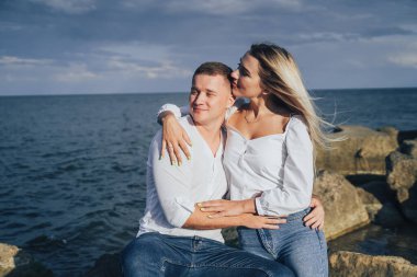 Düşük ihtimal. Mavi bulutlu gökyüzüne karşı denizde taşların üzerinde duran parlak elbiseli çekici bir çift. Yumuşak akşam güneşinin altında. Dört gözle bekliyorum, sarılıyorum, öpüyorum ve güzel bir akşamın tadını çıkarıyorum.