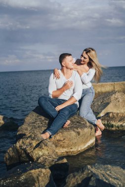 Düşük ihtimal. Mavi bulutlu gökyüzüne karşı denizde taşların üzerinde duran parlak elbiseli çekici bir çift. Yumuşak akşam güneşinin altında. Dört gözle bekliyorum, sarılıyorum, öpüyorum ve güzel bir akşamın tadını çıkarıyorum.