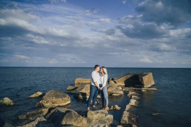 Düşük ihtimal. Mavi bulutlu gökyüzüne karşı denizde taşların üzerinde duran parlak elbiseli çekici bir çift. Yumuşak akşam güneşinin altında. Dört gözle bekliyorum, sarılıyorum, öpüyorum ve güzel bir akşamın tadını çıkarıyorum.