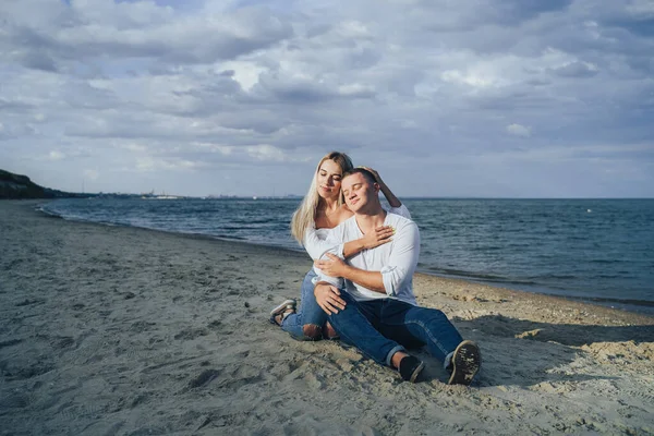 Lifestyle romantic evening for two. Young lovers went on a trip to the sea. Sitting on the sand in the evening sun and hugging, talking, kissing and enjoying the absence of people around.