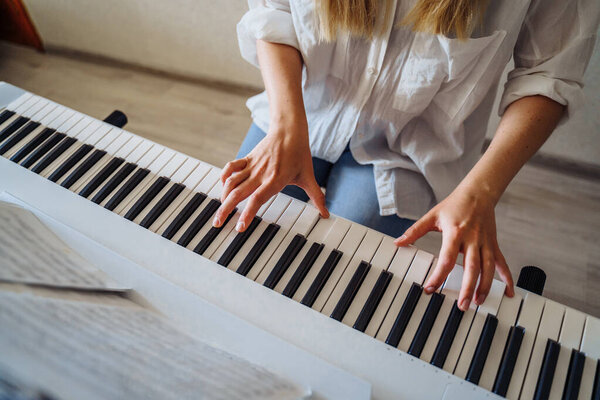 Женщина помещена в карантин на домашнем коронавирусе. Привлекательная девушка в белой рубашке и джинсах сидит дома на самоизоляции и играет на электронном пианино - синтезаторе. Хобби - что делать дома
?