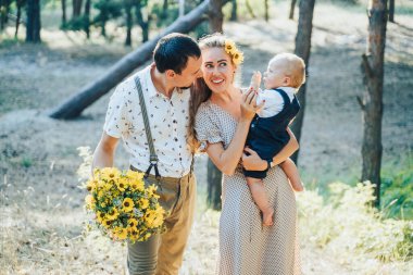 Güzel bir aile yaz ormanında yürüyor. Mutlu ebeveynler temiz havanın ve güzel doğanın tadını çıkarıyorlar, el ele tutuşuyorlar, konuşuyorlar, gülüyorlar ve gülüyorlar. Sağlıklı bir yaşam tarzı. Ebeveynler güneşe bakar ve konuşurlar.