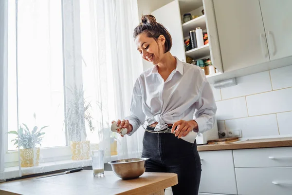 DIY home cooking concept. A bright brunette woman sifting the flour for pancakes through a sieve, salting the dough, adding milk. Young woman smiling, loves to cook in a beautiful modern kitchen.