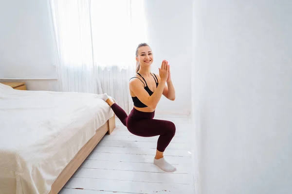 That\'s how it should be! Flexible, muscular, athlete girl does stretching, lifting leg up to the wall. Fitness trainer making a twine at home in the bedroom. Conducting live broadcasts for students