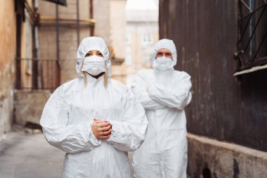 Koruyucu giysili ve koruyucu maskeli doktorlar sokakta ciddi yüzleri olan dururlar. Sokakta yürürken, adam kadını ileriye doğru götürüyor. Çok kararlılar. Coronirus covid-19 konsepti